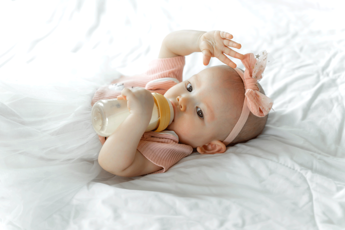 baby-drinks-milk-from-bottle-white-bed.png